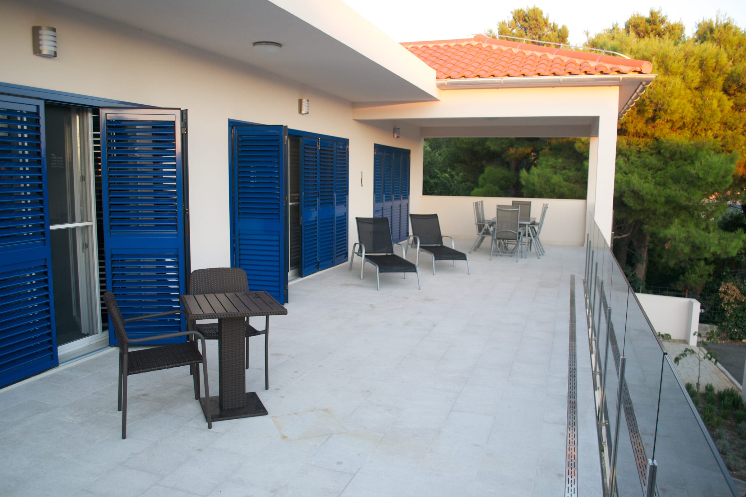 The upper terrace, with a table and chairs, sun loungers and blue louvred shutters along the wall